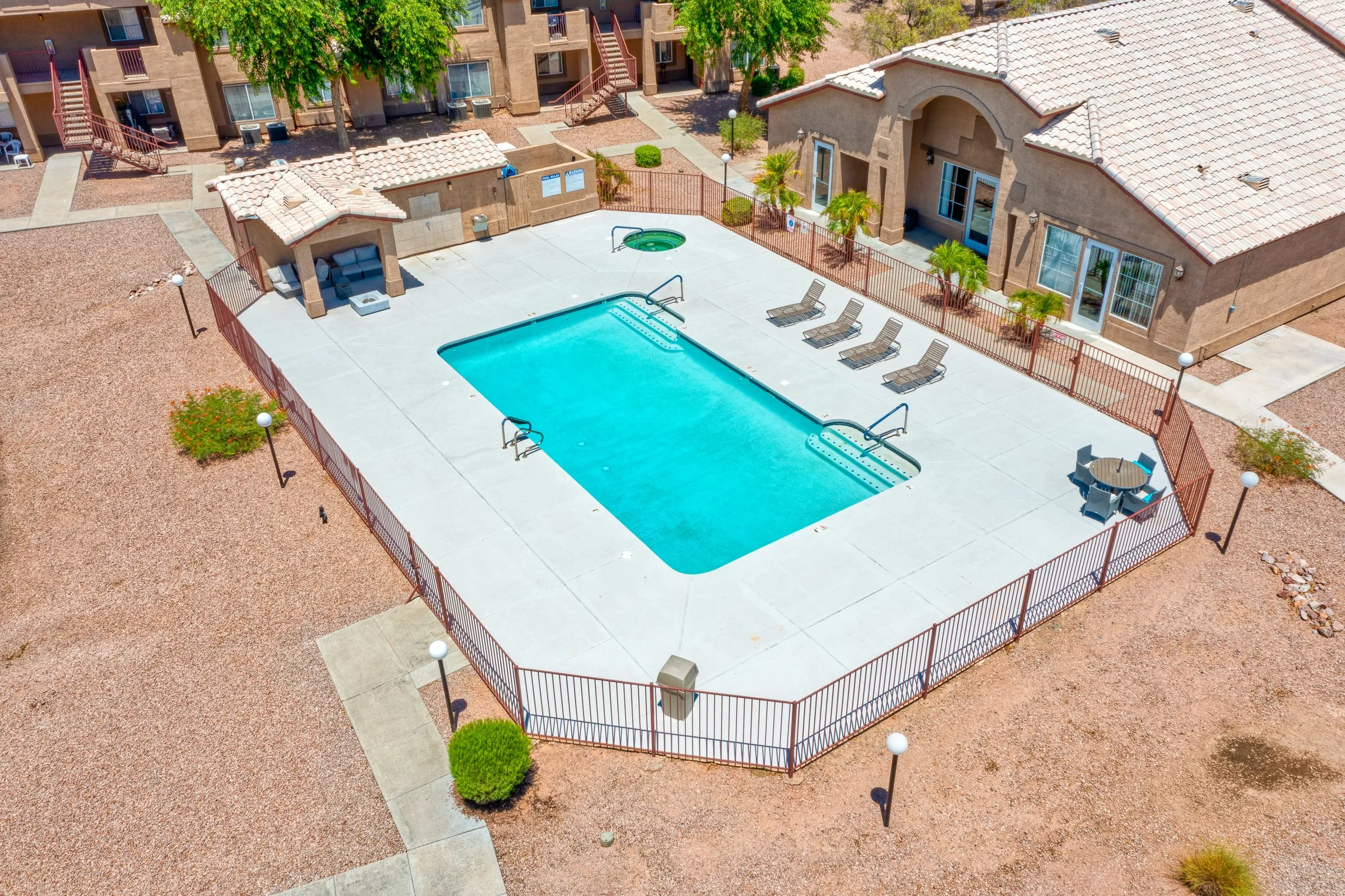 Angled aerial view of a bright turquoise community pool beside a tile-roofed clubhouse.