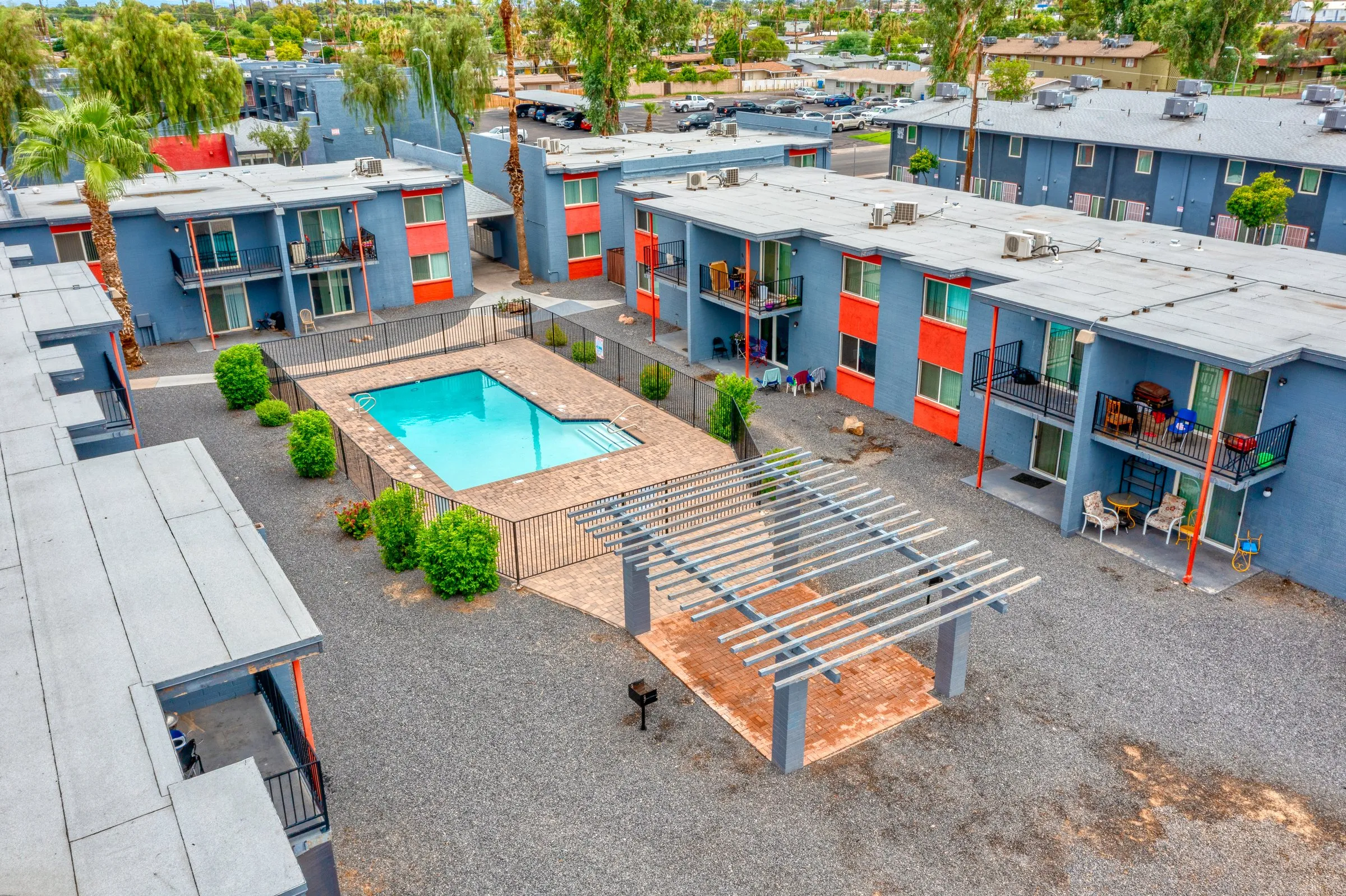 Aerial view of a blue apartment courtyard with a pool, pergola and orange doors.