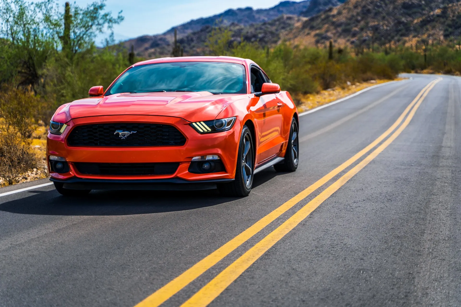 Orange sports car on a desert road with double yellow lines and mountains behind.