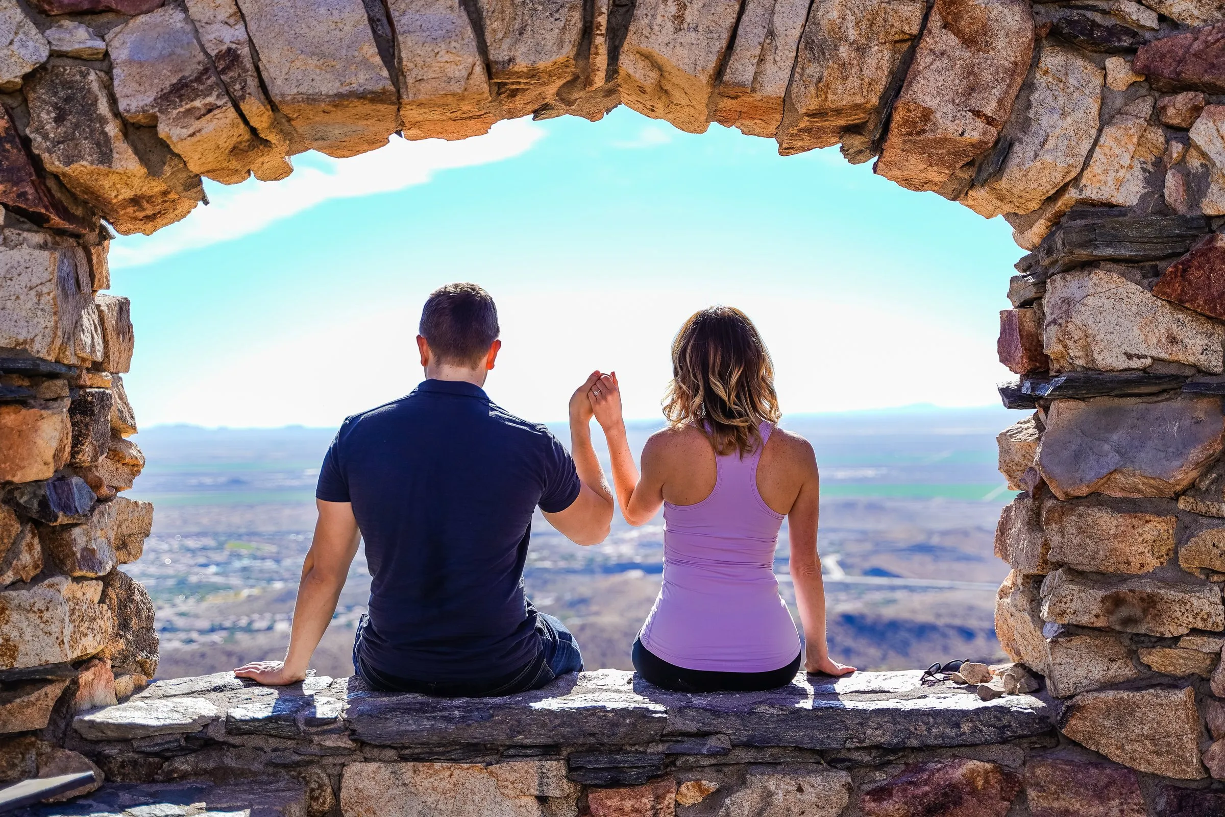 Two people seated from behind in a stone arch overlooking a desert valley.