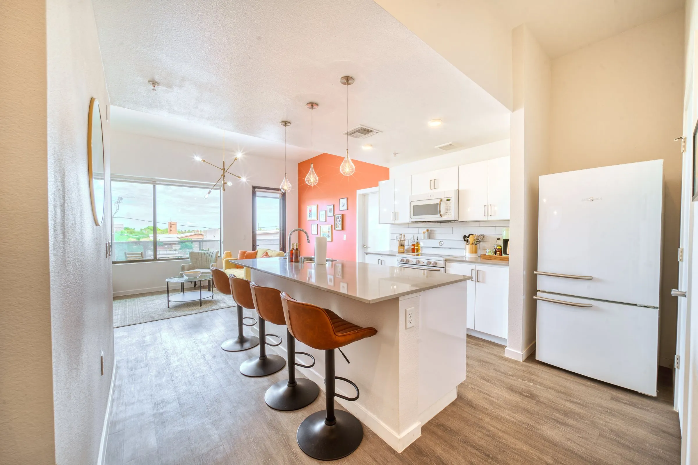 Open-plan kitchen with white cabinets, a long island and orange bar stools.